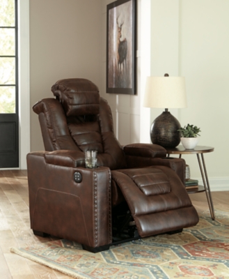 When it comes to style, you’ve got game. Rest assured, the Owner’s Box power recliner is sure to win you over with its ultra-cool looks and major league features. Showcasing all the bells and whistles, this designer recliner is inspired by sports car interiors—with a fabulous faux leather accentuated with horizontal channel tufting. An advanced one-touch power control with an Easy View™ power headrest puts you in the driver’s seat. Dual cup holders and armrests with hidden storage take the form and function to another level.One-touch power control with adjustable positions | Easy View™ adjustable headrest | Corner-blocked frame with metal reinforced seat | Attached cushions | High-resiliency foam cushions wrapped in thick poly fiber | Faux leather upholstery | Each armrest includes storage compartment and cup holder | Extended ottoman for enhanced comfort | Power cord included; UL Listed | Exposed feet with faux wood finish | Estimated Assembly Time: 15 Minutes