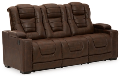 When it comes to style, you’ve got game. Rest assured, the Owner’s Box power reclining sofa is sure to win you over with its ultra-cool looks and major league features. Showcasing all the bells and whistles, this designer reclining sofa is inspired by sports car interiors—with a fabulous faux leather accentuated with horizonal channel tufting. An advanced one-touch power control with an Easy View™ power headrest puts you in the driver’s seat. Dual cup holders and armrests with hidden storage take the form and function to another level, while a middle seat with drop-down table, cup holders and docking station cater to your every want and need.Dual-sided recliner | One-touch power control with adjustable positions | Easy View™ adjustable headrest | Corner-blocked frame with metal reinforced seat | Attached cushions | High-resiliency foam cushions wrapped in thick poly fiber | Faux leather upholstery | Each armrest includes storage compartment and cup holder | Extended ottoman for enhanced comfort | Drop down table with 2 cup holders plus A/C power and USB ports for charging electronics | Power cord included; UL Listed | Exposed feet with faux wood finish | Estimated Assembly Time: 15 Minutes