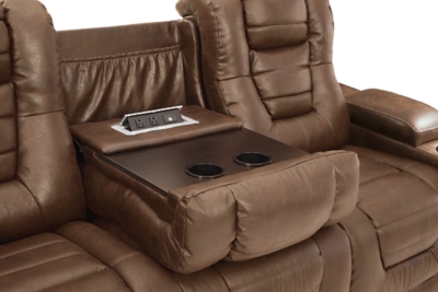 When it comes to style, you’ve got game. Rest assured, the Owner’s Box power reclining sofa is sure to win you over with its ultra-cool looks and major league features. Showcasing all the bells and whistles, this designer reclining sofa is inspired by sports car interiors—with a fabulous faux leather accentuated with horizonal channel tufting. An advanced one-touch power control with an Easy View™ power headrest puts you in the driver’s seat. Dual cup holders and armrests with hidden storage take the form and function to another level, while a middle seat with drop-down table, cup holders and docking station cater to your every want and need.Dual-sided recliner | One-touch power control with adjustable positions | Easy View™ adjustable headrest | Corner-blocked frame with metal reinforced seat | Attached cushions | High-resiliency foam cushions wrapped in thick poly fiber | Faux leather upholstery | Each armrest includes storage compartment and cup holder | Extended ottoman for enhanced comfort | Drop down table with 2 cup holders plus A/C power and USB ports for charging electronics | Power cord included; UL Listed | Exposed feet with faux wood finish | Estimated Assembly Time: 15 Minutes