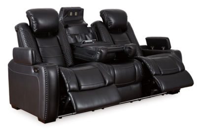 The Party Time power reclining sofa takes its cue from luxury automobiles with lattice- and cross-hatch stitching, for a richly tailored aesthetic that gives you plenty of reasons to celebrate. Sumptuously padded cushions and dramatic midnight black faux leather upholstery add to the indulgence. When it’s time to rev up the action, the sofa’s dual reclining bucket seats (middle seat is stationary), Easy View™ power adjustable headrests and center seat that folds down into a table keep you in the driver’s seat. Ambient blue LED lighting on the base and cup holders completes the theater-style experience.Dual-sided recliner | Polyester/polyurethane upholstery | Corner-blocked frame with metal reinforced seats | Attached backs and seat cushions | High-resiliency foam cushions wrapped in thick poly fiber | One-touch power controls with adjustable positions | Easy View™ power adjustable headrests | Flip up padded armrests with hidden storage underneath | Drop down table with 2 cup holders and a handy docking station for charging electronics | Includes USB charging port in each power control | Flip up LED light (under center seat headrest) | LED lighting on the base and cup holders for theater-style experience | Power cord included; UL Listed | Estimated Assembly Time: 15 Minutes