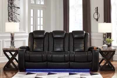 The Party Time power reclining sofa takes its cue from luxury automobiles with lattice- and cross-hatch stitching, for a richly tailored aesthetic that gives you plenty of reasons to celebrate. Sumptuously padded cushions and dramatic midnight black faux leather upholstery add to the indulgence. When it’s time to rev up the action, the sofa’s dual reclining bucket seats (middle seat is stationary), Easy View™ power adjustable headrests and center seat that folds down into a table keep you in the driver’s seat. Dual-sided recliner | One-touch power controls with adjustable positions | Easy View™ power adjustable headrests | Corner-blocked frame with metal reinforced seats | Attached backs and seat cushions | High-resiliency foam cushions wrapped in thick poly fiber | Polyester/polyurethane upholstery | Flip up padded armrests with hidden storage underneath | Drop down table with 2 cup holders and a handy docking station for charging electronics | Includes USB charging port in each power control | Flip up LED light (under center seat headrest) | Ambient blue LED lighting on cup holders and base for a theater-style experience | Power cord included; UL Listed | Estimated Assembly Time: 15 Minutes