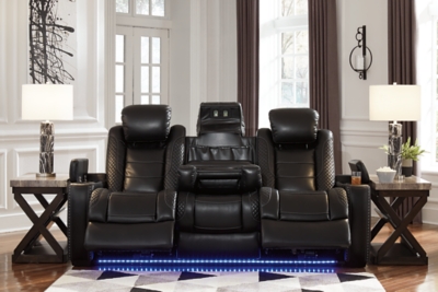 The Party Time power reclining sofa takes its cue from luxury automobiles with lattice- and cross-hatch stitching, for a richly tailored aesthetic that gives you plenty of reasons to celebrate. Sumptuously padded cushions and dramatic midnight black faux leather upholstery add to the indulgence. When it’s time to rev up the action, the sofa’s dual reclining bucket seats (middle seat is stationary), Easy View™ power adjustable headrests and center seat that folds down into a table keep you in the driver’s seat. Ambient blue LED lighting on the base and cup holders completes the theater-style experience.Dual-sided recliner | Polyester/polyurethane upholstery | Corner-blocked frame with metal reinforced seats | Attached backs and seat cushions | High-resiliency foam cushions wrapped in thick poly fiber | One-touch power controls with adjustable positions | Easy View™ power adjustable headrests | Flip up padded armrests with hidden storage underneath | Drop down table with 2 cup holders and a handy docking station for charging electronics | Includes USB charging port in each power control | Flip up LED light (under center seat headrest) | LED lighting on the base and cup holders for theater-style experience | Power cord included; UL Listed | Estimated Assembly Time: 15 Minutes