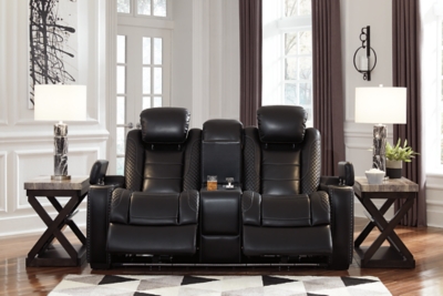 The Party Time power reclining loveseat takes its cue from luxury automobiles with lattice- and cross-hatch stitching, for a richly tailored aesthetic that gives you plenty of reasons to celebrate. Sumptuously padded cushions and dramatic midnight black faux leather upholstery add to the indulgence. When it’s time to rev up the action, the loveseat’s dual reclining bucket seats, Easy View™ power adjustable headrests and center console keep you in the driver’s seat. Dual-sided recliner | One-touch power controls with adjustable positions | Easy View™ power adjustable headrests | Corner-blocked frame with metal reinforced seats | Attached backs and seat cushions | High-resiliency foam cushions wrapped in thick poly fiber | Polyester/polyurethane upholstery | Includes USB charging port in each power control | Flip up padded armrests with hidden storage | Center console with cup holders and underneath storage | Ambient blue LED lighting on cup holders and base for a theater-style experience | Power cord included; UL Listed | Estimated Assembly Time: 15 Minutes