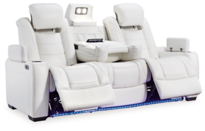 The Party Time power reclining sofa takes its cue from luxury automobiles with lattice and crosshatch stitching, for a richly tailored aesthetic that gives you plenty of reasons to celebrate. Sumptuously padded cushions and crisp white faux leather upholstery add to the indulgence. When it’s time to rev up the action, the dual reclining bucket seats (middle seat is stationary), Easy View™ power adjustable headrests and a center seat that folds down into a table keep you in the driver’s seat. Ambient blue LED lighting on the base and cup holders completes the theater-style experience.Dual-sided recliner | Polyester/polyurethane upholstery | Corner-blocked frame with metal reinforced seat | Attached back and seat cushions | High-resiliency foam cushions wrapped in thick poly fiber | One-touch power control with adjustable positions, Easy View™ adjustable headrest and USB plug-in | Flip up padded armrests with hidden storage | Drop down table with 2 cup holders and a handy docking station for charging electronics | Flip up LED light (under center seat headrest) | LED lighting on cup holders and base for theater-style experience | Power cord included; UL Listed | Estimated Assembly Time: 15 Minutes
