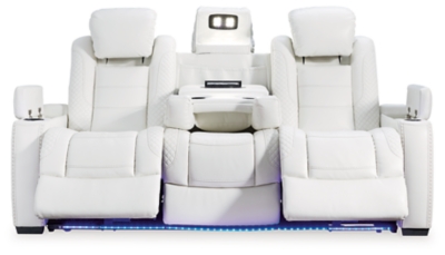 The Party Time power reclining sofa takes its cue from luxury automobiles with lattice and crosshatch stitching, for a richly tailored aesthetic that gives you plenty of reasons to celebrate. Sumptuously padded cushions and crisp white faux leather upholstery add to the indulgence. When it’s time to rev up the action, the dual reclining bucket seats (middle seat is stationary), Easy View™ power adjustable headrests and a center seat that folds down into a table keep you in the driver’s seat.Dual-sided recliner | Polyester/polyurethane upholstery | Corner-blocked frame with metal reinforced seat | Attached back and seat cushions | High-resiliency foam cushions wrapped in thick poly fiber | One-touch power control with adjustable positions, Easy View™ adjustable headrest and USB plug-in | Flip up padded armrests with hidden storage | Drop down table with 2 cup holders and a handy docking station for charging electronics | Flip up LED light (under center seat headrest) | Ambient blue LED lighting on cup holders and base for a theater-style experience | Power cord included; UL Listed | Estimated Assembly Time: 15 Minutes