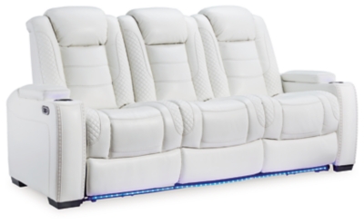 The Party Time power reclining sofa takes its cue from luxury automobiles with lattice and crosshatch stitching, for a richly tailored aesthetic that gives you plenty of reasons to celebrate. Sumptuously padded cushions and crisp white faux leather upholstery add to the indulgence. When it’s time to rev up the action, the dual reclining bucket seats (middle seat is stationary), Easy View™ power adjustable headrests and a center seat that folds down into a table keep you in the driver’s seat.Dual-sided recliner | Polyester/polyurethane upholstery | Corner-blocked frame with metal reinforced seat | Attached back and seat cushions | High-resiliency foam cushions wrapped in thick poly fiber | One-touch power control with adjustable positions, Easy View™ adjustable headrest and USB plug-in | Flip up padded armrests with hidden storage | Drop down table with 2 cup holders and a handy docking station for charging electronics | Flip up LED light (under center seat headrest) | Ambient blue LED lighting on cup holders and base for a theater-style experience | Power cord included; UL Listed | Estimated Assembly Time: 15 Minutes