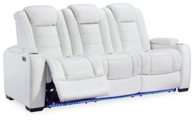 The Party Time power reclining sofa takes its cue from luxury automobiles with lattice and crosshatch stitching, for a richly tailored aesthetic that gives you plenty of reasons to celebrate. Sumptuously padded cushions and crisp white faux leather upholstery add to the indulgence. When it’s time to rev up the action, the dual reclining bucket seats (middle seat is stationary), Easy View™ power adjustable headrests and a center seat that folds down into a table keep you in the driver’s seat. Ambient blue LED lighting on the base and cup holders completes the theater-style experience.Dual-sided recliner | Polyester/polyurethane upholstery | Corner-blocked frame with metal reinforced seat | Attached back and seat cushions | High-resiliency foam cushions wrapped in thick poly fiber | One-touch power control with adjustable positions, Easy View™ adjustable headrest and USB plug-in | Flip up padded armrests with hidden storage | Drop down table with 2 cup holders and a handy docking station for charging electronics | Flip up LED light (under center seat headrest) | LED lighting on cup holders and base for theater-style experience | Power cord included; UL Listed | Estimated Assembly Time: 15 Minutes