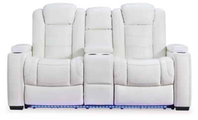 The Party Time power reclining loveseat takes its cue from luxury automobiles with lattice and crosshatch stitching, for a richly tailored aesthetic that gives you plenty of reasons to celebrate. Sumptuously padded cushions and crisp white faux leather upholstery add to the indulgence. When it’s time to rev up the action, the dual reclining bucket seats, Easy View™ power adjustable headrests and center console with docking station keep you in the driver’s seat. Dual-sided recliner | Polyester/polyurethane upholstery | Corner-blocked frame with metal reinforced seat | Attached back and seat cushions | High-resiliency foam cushions wrapped in thick poly fiber | One-touch power control with adjustable positions, Easy View™ adjustable headrest and USB plug-in | Flip up padded armrests with hidden storage | Center console with cup holders and underneath storage | Ambient blue LED lighting on cup holders and base for a theater-style experience | Power cord included; UL Listed | Estimated Assembly Time: 15 Minutes