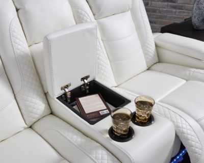 The Party Time power reclining loveseat takes its cue from luxury automobiles with lattice and crosshatch stitching, for a richly tailored aesthetic that gives you plenty of reasons to celebrate. Sumptuously padded cushions and crisp white faux leather upholstery add to the indulgence. When it’s time to rev up the action, the dual reclining bucket seats, Easy View™ power adjustable headrests and center console with docking station keep you in the driver’s seat. Dual-sided recliner | Polyester/polyurethane upholstery | Corner-blocked frame with metal reinforced seat | Attached back and seat cushions | High-resiliency foam cushions wrapped in thick poly fiber | One-touch power control with adjustable positions, Easy View™ adjustable headrest and USB plug-in | Flip up padded armrests with hidden storage | Center console with cup holders and underneath storage | Ambient blue LED lighting on cup holders and base for a theater-style experience | Power cord included; UL Listed | Estimated Assembly Time: 15 Minutes