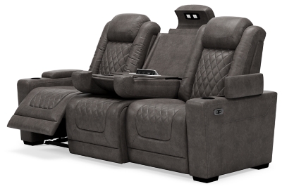 The Hyllmont power reclining sofa in trendy gray is proof of just how far recliners have come when it comes to form and function. Ultra cool and contemporary, this fully loaded power reclining sofa makes it so easy to social distance and make home your haven. Dressed to impress with diamond stitching inspired by sports car interiors, this reclining sofa is covered in a fabulous faux leather with pebbled effect for authenticity. High-tech advancements include a one-touch power control with Easy View™ adjustable headrest and USB plug-in and a drop-down table with cup holders, flip-up light and AC power/USB plug-ins. Dual-sided recliner | One-touch power control with adjustable positions, Easy View™ adjustable headrest and USB plug-in | Corner-blocked frame with metal reinforced seat | Attached cushions | High-resiliency foam cushions wrapped in thick poly fiber | Each armrest with hidden storage and cup holder | Drop-down center table with 2 cup holders, flip-up light and hidden AC power and USB ports | Faux leather polyester upholstery | Power cord included; UL Listed | Exposed tapered feet | Estimated Assembly Time: 15 Minutes