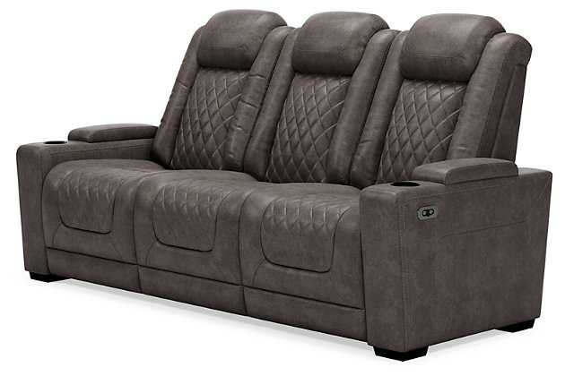 The Hyllmont power reclining sofa in trendy gray is proof of just how far recliners have come when it comes to form and function. Ultra cool and contemporary, this fully loaded power reclining sofa makes it so easy to social distance and make home your haven. Dressed to impress with diamond stitching inspired by sports car interiors, this reclining sofa is covered in a fabulous faux leather with pebbled effect for authenticity. High-tech advancements include a one-touch power control with Easy View™ adjustable headrest and USB plug-in and a drop-down table with cup holders, flip-up light and AC power/USB plug-ins. Dual-sided recliner | One-touch power control with adjustable positions, Easy View™ adjustable headrest and USB plug-in | Corner-blocked frame with metal reinforced seat | Attached cushions | High-resiliency foam cushions wrapped in thick poly fiber | Each armrest with hidden storage and cup holder | Drop-down center table with 2 cup holders, flip-up light and hidden AC power and USB ports | Faux leather polyester upholstery | Power cord included; UL Listed | Exposed tapered feet | Estimated Assembly Time: 15 Minutes