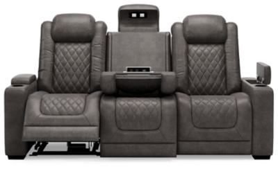 The Hyllmont power reclining sofa in trendy gray is proof of just how far recliners have come when it comes to form and function. Ultra cool and contemporary, this fully loaded power reclining sofa makes it so easy to social distance and make home your haven. Dressed to impress with diamond stitching inspired by sports car interiors, this reclining sofa is covered in a fabulous faux leather with pebbled effect for authenticity. High-tech advancements include a one-touch power control with Easy View™ adjustable headrest and USB plug-in and a drop-down table with cup holders, flip-up light and AC power/USB plug-ins. Dual-sided recliner | One-touch power control with adjustable positions, Easy View™ adjustable headrest and USB plug-in | Corner-blocked frame with metal reinforced seat | Attached cushions | High-resiliency foam cushions wrapped in thick poly fiber | Each armrest with hidden storage and cup holder | Drop-down center table with 2 cup holders, flip-up light and hidden AC power and USB ports | Faux leather polyester upholstery | Power cord included; UL Listed | Exposed tapered feet | Estimated Assembly Time: 15 Minutes