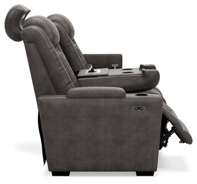 The Hyllmont power reclining sofa in trendy gray is proof of just how far recliners have come when it comes to form and function. Ultra cool and contemporary, this fully loaded power reclining sofa makes it so easy to social distance and make home your haven. Dressed to impress with diamond stitching inspired by sports car interiors, this reclining sofa is covered in a fabulous faux leather with pebbled effect for authenticity. High-tech advancements include a one-touch power control with Easy View™ adjustable headrest and USB plug-in and a drop-down table with cup holders, flip-up light and AC power/USB plug-ins. Dual-sided recliner | One-touch power control with adjustable positions, Easy View™ adjustable headrest and USB plug-in | Corner-blocked frame with metal reinforced seat | Attached cushions | High-resiliency foam cushions wrapped in thick poly fiber | Each armrest with hidden storage and cup holder | Drop-down center table with 2 cup holders, flip-up light and hidden AC power and USB ports | Faux leather polyester upholstery | Power cord included; UL Listed | Exposed tapered feet | Estimated Assembly Time: 15 Minutes