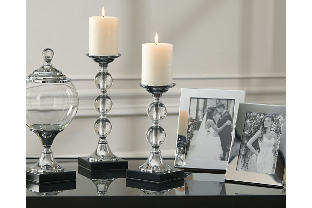 Bring some shine to your decor with the Diella 5-piece accessory set. Candle holders made of real crystal and silvertone metal give your space a high-end appeal. You’ll love putting your most adored photos in the silvertone frames. Step things up one more level with the glass and metal globe-shaped box. What a great mix for the bold interior decorator.Includes lidded box, 2 candle holders, 2 photo frames (large and small) and 2 vases (large and small) | Made of silvertone metal, glass and crystal | Candler holder holds 3" pillar candle (not included) | Clean with a soft, dry cloth