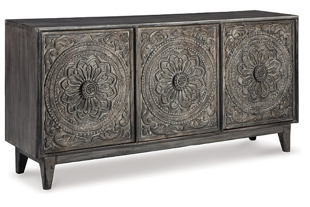Have a taste for something exotic? Feast your eyes on the exquisitely styled Fair Ridge console. Whether tantalizing in the dining room, gracing an entryway or serving as an eclectic TV stand—what a masterpiece of an accent piece. Fancifully floral-carved doors are a striking contrast to the console’s ultra-linear profile.Made of solid wood | Hand-carved accents | 3 shelves behind 3 cabinet doors | Antique gray finish | Includes tipping restraint pack | Excluded from promotional discounts and coupons | Estimated Assembly Time: 15 Minutes