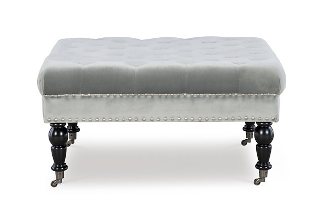 Square tufted ottoman on metal casters brings high style and versatility to your living space. Perfect as a footrest or coffee table, it wows with a tufted top and velvety soft gray fabric. Brushed silvertone nailheads accent the side, while turned black legs complete the richly traditional look.Made of birch wood | Foam cushioned seat covered in velvet polyester upholstery | Tufted top | Brushed silvertone nailhead trim | Black finished legs | Metal casters | Assembly required