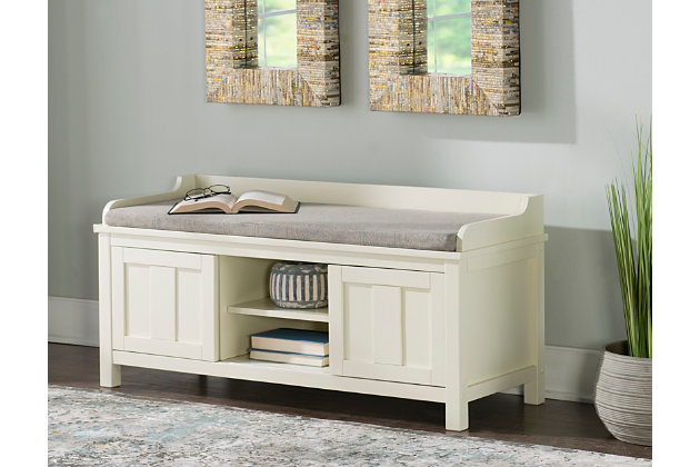 Whether gracing a front entry, living room, kitchen or mudroom, this storage bench is loaded with vintage charm. The bench’s plush cushion adds comfort to the seat, and ample bottom storage offers space for shoes, books and catchalls. Sliding doors keep your items hidden from sight, while the cream finish is an easy addition to any space.Made of wood, engineered wood, foam and fabric | Antiqued cream color finish | 2 sliding doors | 1 fixed shelf | Foam-filled cushion in gray polyester linen fabric | Assembly required