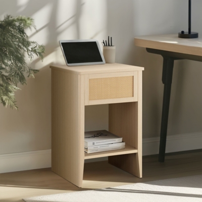 Wooden nightstand with woven front panel and open lower shelf, set in a home office area with desk and plant.