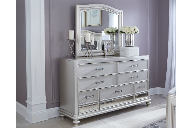 The Coralayne dresser and mirror set allures with the glitz and glam befitting silver screen queens. Exquisite frame's metallic tone channels that Hollywood Regency flair you've been dreaming of. Faux shagreen texturing on the drawer fronts, a touch of bejeweling on the sculptural pulls and a strip of mirror sheen elevate Coralayne to interior fashion's A list.Made of veneers, wood and engineered wood | Metallic sheen finish | Faux shagreen drawer fronts | Mirror border detailing | Chrome-tone pulls with faux crystal bejeweling | 7 smooth-gliding drawers with dovetail construction and metal ball bearing slides | 3 top drawers felt lined | Mirror attaches to back of dresser | Assembly required | Includes tipover restraint device | Estimated Assembly Time: 35 Minutes