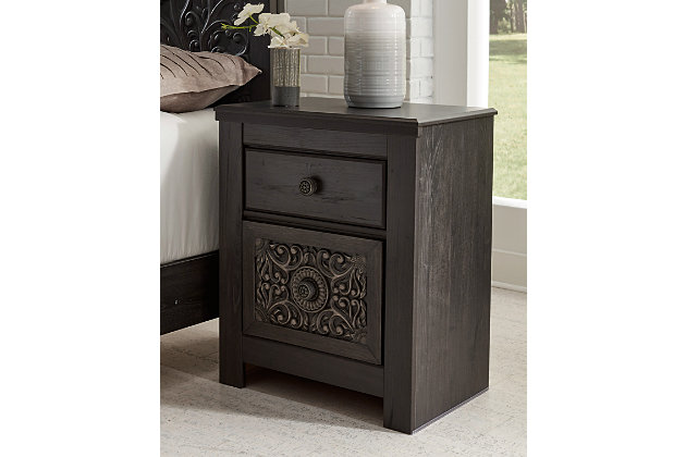Showcase your trend-setting spirit with the Paxberry nightstand. Inspired by bohemian tapestries, exquisite carved medallion pattern is a testament to boho-chic style. Sophisticated dark finish sets a foundation for a room bursting with personality. Best of all, nightstand includes handy USB charging ports.Made of engineered wood (MDF/particleboard) and decorative laminate | Vintage aged black/brown finish over replicated oak grain | Hardware features a worn-through painted effect | 2 smooth-gliding drawers with faux linen lining | USB chargers | Power cord included; UL Listed | Assembly required