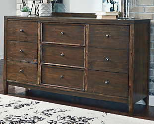 If you’re longing for just the right blend of high-style contemporary and mid-century minimalism, the Kisper dresser rises to the occasion. A mastery in simplicity, this dresser is ready to impress with a brushed dry-brown wood finish that’s wonderfully complex. Framed drawer accents and a wire-brushed texture give this richly veneered piece added interest. “Off-the-floor” design beautifully elevates the mood.Dresser only | Made of wood, veneers and engineered wood | Brushed dry-brown wood finish | Wire-brushed texture | 9 smooth-gliding drawers with dovetail construction (top drawers felt lined) | Includes tipover restraint device | Estimated Assembly Time: 15 Minutes
