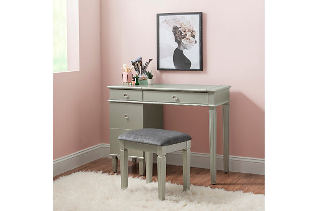 This alluring vanity exudes feminine style and glamorous design. The vanity features a flip top that reveals a hidden mirror and interior storage space. Spacious drawers provide ample storage for accessories, makeup and more. Clear decorative knobs and beaded trim complete the front of the piece. Finished in chic silvertone, this vanity set will easily complement a variety of existing colors. Matching stool is upholstered in a gray polyester fabric. Perfect for a bedroom or dressing area.Includes vanity with hidden mirror and upholstered stool | Made of wood, hardwood and engineered wood with mirrored glass | Silvertone finish with beaded trim | Padded seat with gray polyester upholstery | 3 drawers with clear decorative knobs | Large bottom drawer with salon-style slots for your brushes, curling iron, hairdryer, etc. | Jewelry tray | Some assembly required