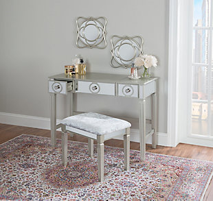 Add a glamourous touch to the room or dressing area with the Renay vanity set. Finished in silver and designed in grand elegance, you'll discover attractive elements like tapered legs with reeds and a mirrored front accented by round silver pulls. The matching stool also has mirrored details and its padded seat is upholstered in gray fabric upholstery. The vanity's mirror can be flipped down when not in use providing you with tabletop space. Plus, three drawers offer hidden storage—perfect for keeping the room tidy.Made of rubberwood, engineered wood and mirror | Silver finish with mirrored front | Flip top mirror | 3 drawers with round silvertone pulls | Includes padded stool upholstered in gray fabric | Tapered, reeded legs | Assembly required