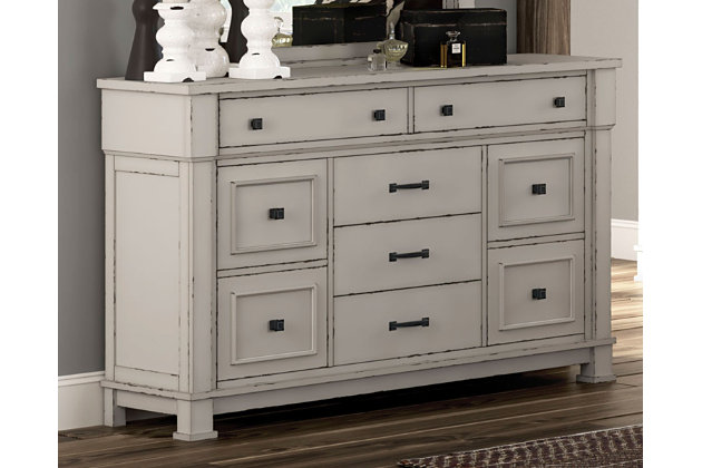 Given just enough distressing for family heirloom charm, the Jennily dresser is a mastery in modern farmhouse style. The ultimate choice for a dreamy bedroom retreat, its antiqued white finish is wonderfully easy on the eyes. Sturdy silhouette with bold pilasters gives this 9-drawer dresser such a rich, substantial presence. Various drawer sizes nicely accommodate, while combination of flush mount and framed drawer fronts is an inspired touch.Dresser only | Made of wood and engineered wood | Antiqued white finish | Rubbed dark metal hardware | 9 smooth-gliding drawers | Top 2 drawers felt lined | Includes tipover restraint device | Estimated Assembly Time: 15 Minutes