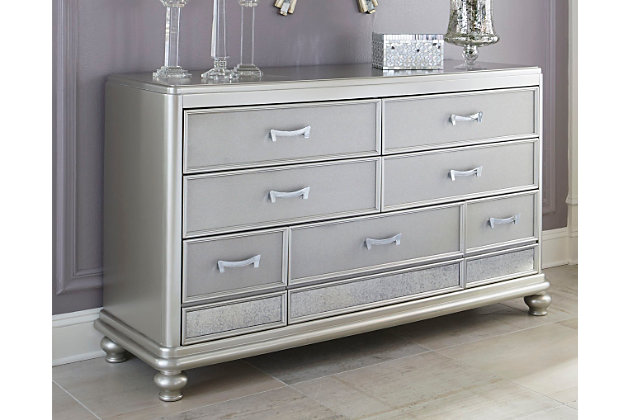 The Coralayne dresser allures with the glitz and glam befitting silver screen queens. Exquisite frame's metallic tone channels that Hollywood Regency flair you've been dreaming of. Faux shagreen texturing on the drawer fronts, a touch of bejeweling on the sculptural pulls and a strip of mirror sheen elevate Coralayne to interior fashion's A list.Dresser only | Made of veneers, wood and engineered wood | Metallic sheen finish | Faux shagreen drawer fronts | Mirror border detailing | Chrome-tone pulls with faux crystal bejeweling | 7 smooth-gliding drawers with dovetail construction and metal ball bearing slides | 2 top drawers felt lined | Includes tipover restraint device | Estimated Assembly Time: 15 Minutes
