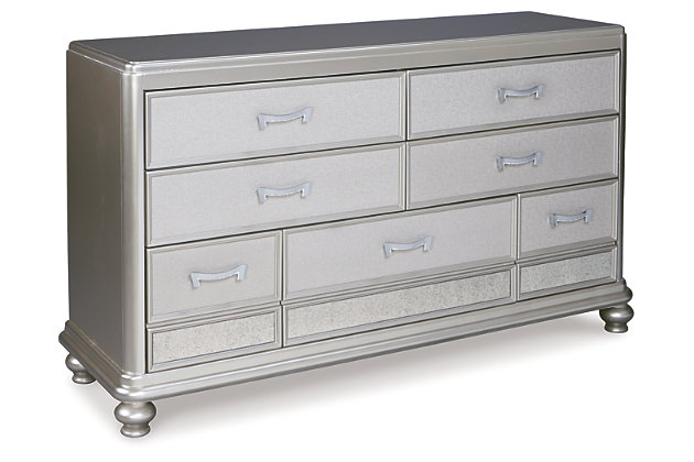 The Coralayne dresser allures with the glitz and glam befitting silver screen queens. Exquisite frame's metallic tone channels that Hollywood Regency flair you've been dreaming of. Faux shagreen texturing on the drawer fronts, a touch of bejeweling on the sculptural pulls and a strip of mirror sheen elevate Coralayne to interior fashion's A list.Dresser only | Made of veneers, wood and engineered wood | Metallic sheen finish | Faux shagreen drawer fronts | Mirror border detailing | Chrome-tone pulls with faux crystal bejeweling | 7 smooth-gliding drawers with dovetail construction and metal ball bearing slides | 2 top drawers felt lined | Includes tipover restraint device | Estimated Assembly Time: 15 Minutes