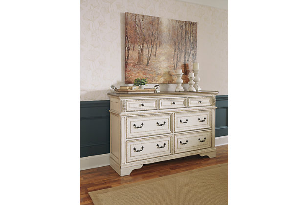 Elevating the art of traditional cottage styling, the Realyn dresser is your dream bedroom retreat realized. Antiqued two-tone aesthetic blends a chipped white with a distressed wood finished top for added charm. Framed drawer fronts and decorative corbels add refinement, while bail pulls in a dark bronze-tone finish lend a classic touch.Dresser only | Made of wood, engineered wood and veneers, with cast resin components | Antiqued two-tone finish | Dark bronze-tone finished metal hardware | 7 smooth-gliding drawers with dovetail construction | Includes tipover restraint device | Estimated Assembly Time: 15 Minutes