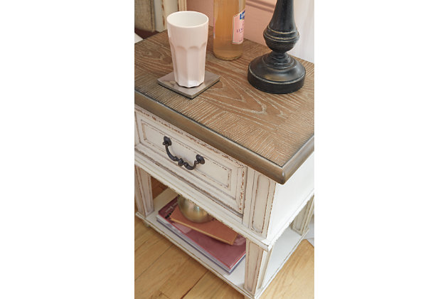 Elevating the art of traditional cottage styling, the Realyn nightstand is your dream bedroom retreat realized. Antiqued two-tone aesthetic blends a chipped white with a distressed wood finished top for added charm. Adorned with classic bail pull hardware, the smooth-gliding drawer is crafted with quality dovetail construction for years of satisfaction.Made of veneers, wood and engineered wood | Antiqued two-tone finish | Smooth-gliding drawer with dovetail construction | Dark bronze-tone finished metal hardware | Open display shelf | Estimated Assembly Time: 15 Minutes