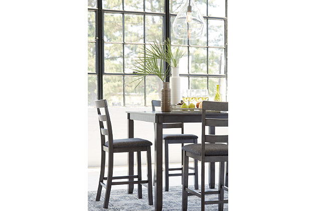 It’s so easy being gray—at least the Bridson 5-piece dining set makes it seem that way. This transitional counter-height table and barstool ensemble sports a charcoal gray finish with textured gray upholstery for an on-trend and relevant appeal. Plushly upholstered seat cushion in a practical polyfiber makes it a pleasure to linger at the table. Best of all, square table design is ideally suited for small spaces.Includes counter height table and 4 barstools | Made of wood, veneer and engineered wood | Medium charcoal gray finish | Ladderback barstools | Cushioned seats covered in textured gray polyester upholstery | Table with tapered leg design | Assembly required | Estimated Assembly Time: 90 Minutes