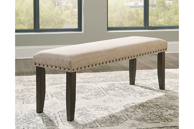 Make gatherings memorable with ever-trendy farmhouse seating. The Rokane dining bench keeps things cozy with light brown textured fabric and a cushioned seat. Punctuated with nailhead trim and the beauty of natural wood grain legs, this urban farmhouse piece is sure to impress come mealtime.Frame and legs are made of solid wood | Rough sawn texture with warm brown finish | Nailhead trim | Polyester upholstery over foam cushioned seat | Assembly required | Estimated Assembly Time: 30 Minutes