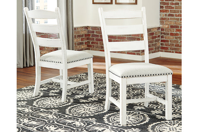 Whether you’re pining for cottage charm or modern farmhouse sophistication, the Valebeck dining room upholstered chair with timeless ladderback styling is something to savor. Distressed vintage white finish exudes a sense of ease that’s all the more enticing thanks to a comfortably cushioned seat wrapped in a soothing gray linen colored textural fabric.Made of solid wood | Distressed vintage white finish with linen colored polyester upholstery | Nailhead trim | Cushioned seat | Assembly required | Estimated Assembly Time: 30 Minutes