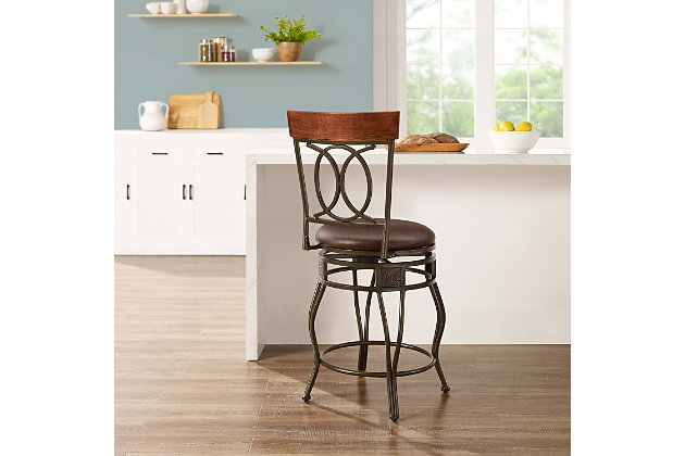 With its scrolled metalwork and fanciful flair, this bar stool with swivel serves up style with a more traditional twist. Complete with a thickly padded seat covered in easy-care vinyl, this swivel bar stool will surely elevate the form and function of a kitchen island area, breakfast bar or entertainment space.Made of bronze-tone metal with wood cap | Brown vinyl upholstery | Foam cushioned seat | Swivel seat | Protective glides under legs | Assembly required