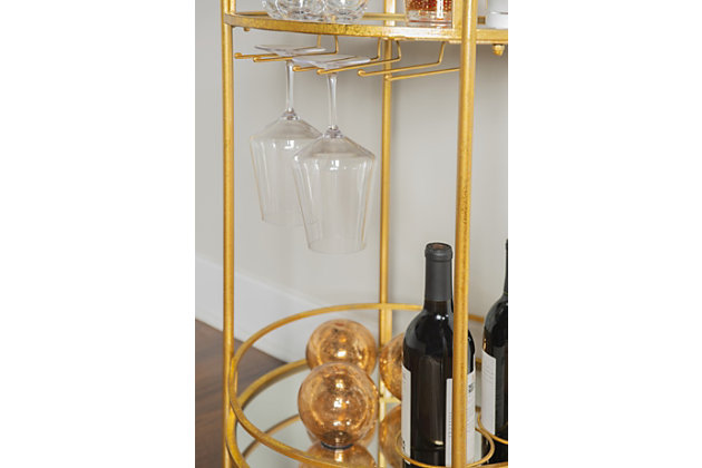 Mixing industrial design with modern flair, the Mayer round bar cart is sure to impress. Showcasing a tubular silhouette cast in a goldtone finish, this charming design features a mirrored shelf with wine glass holders overtop a bottom mirrored shelf with wine bottle holders. Dual handles and wheels allow you to easily transport from room to room, making this home accent perfect for your dining or lounge area.Made of iron and mirrored glass | Goldtone base with gold leaf finish | 2 mirrored shelves | Top shelf with 3 wine glass holders;bottom shelf with 3 wine bottle holders | Casters for easy mobility | 2 handles for easy transport | Diameter of top and shelf: 17.5" | Assembly required
