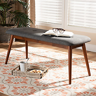 Featuring a stunning medium oak finish, the Flora dining bench brings warmth to any dining space. Constructed from solid rubberwood, it's upholstered in a soft, durable polyester fabric and padded with foam. Expert craftsmanship is displayed in the curved edges and the smooth grained finish. Designed for everyday use, the seat is supported by four angled, tapered legs that create a modern profile while also providing ample legroom. A single row of button tufting adds a decorative touch. The Flora dining bench is made in Malaysia and requires assembly.Mid-century modern dining bench | Foam-padded seat | Medium oak finish | Polyester fabric upholstery | Made of rubberwood | Assembly required