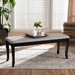 Add casual elegance to your dining room set up with the Cornelie dining bench. This bench is constructed from sturdy wood, with its sleek dark brown finish complementing the soft, gray fabric upholstery. An optimal balance of comfort and style, this bench features a plush foam-padded seat, as well as classic cabriole legs that enable ample leg room. The Cornelie dining bench is well suited for both casual and formal dining.Made of oak wood and rubberwood | Dark brown finish | Upholstered in polyester fabric and padded with foam | Cabriole legs | Assembly required