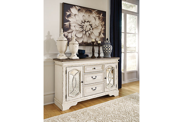 Serve up a French country-inspired feast for the eyes with the Realyn dining room server. Unique elements include cabinet storage beautified with decorative fretwork over mirrored glass and a doubly charming two-tone aesthetic pairing a chipped white with a distressed wood finished top.Made of veneers, wood and engineered wood | Antiqued two-tone finish | 3 smooth-gliding drawers with dovetail construction and felt bottoms | Bail pulls and knobs in dark bronze tone finish | Pair of cabinet doors with inset mirrored glass and decorative fretwork | 2 adjustable shelves | Assembly required | Estimated Assembly Time: 15 Minutes