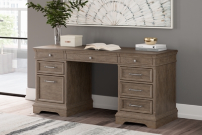 The Janismore Weathered Gray Home Office Storage Leg Desk is available at  Discount Furniture Center proudly serving South Hill and Farmville, VA and  surrounding areas!