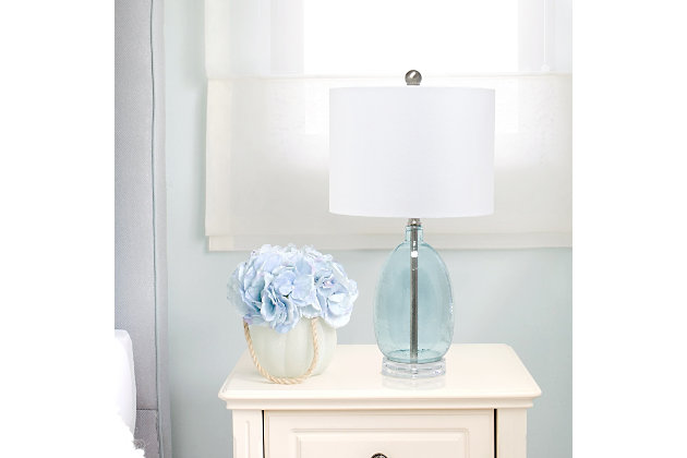 Enhance any room in your home with this simple yet chic table lamp.  The oval shaped base features textured clear blue glass accented with brushed nickel and a white fabric drum shade.  Perfect for your living room, bedroom, office, or anywhere you need to add a tasteful update!Fabric white shade | Textured clear blue glass base | 1 x 60w medium type a base bulb (not included) required | 5 foot clear cord