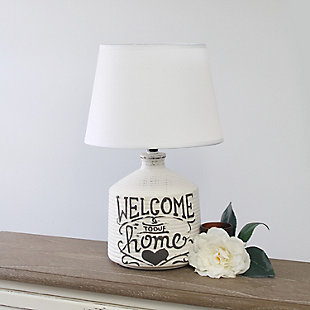 Check out this fine-looking jugular shaped table lamp spruced with a bit of a rustic appeal.  A washed out and slightly unfinished ceramic base is decorated with a black written script and paired with a white linen fabric shade.  In today's world of interior design, this lamp is the farmhouse or countryside lover's ideal lamp find.White wash ridged ceramic base with "welcome to our home" design | White linen empire fabric shade | Uses 1 x 60w type a medium base bulb (not included) | Easy on/off switch located on socket