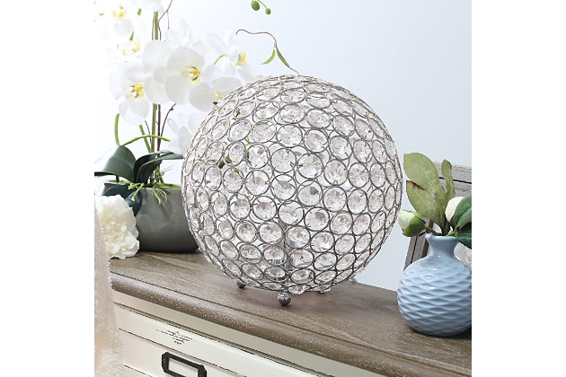 Make your room sparkle with a beautifully designed crystal ball shaped lamp. This 10" version is available in one of the many available finishes is the perfect addition to any bedroom, office, nursery, or even a foyer or entryway! We believe that lighting is like jewelry for your home. Our products will help to enhance your room with elegance and sophistication.Crystal ball shape glows from within casting pretty shadows | Threaded with steel rings and set on ball feet | Chrome finish | Height: 10" diameter:10"