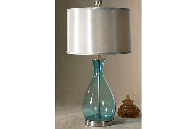 The clear blue mouth-blown glass body of this pretty table lamp coordinates perfectly with the satin nickel-tone metal detail of the neck and base. A silken silver-gray hardback shade adds a sophisticated touch. Perfect for a sofa-side table or reading table, this lamp is sure to complement your decorating scheme no matter where you put it.Made of glass, metal and fabric | Mouth-blown glass body with clear blue finish | Nickel-tone metal finish | Round hardback drum shade with silken silver-gray fabric | 3-way switch | Type a bulb; 150 watts max (not included)