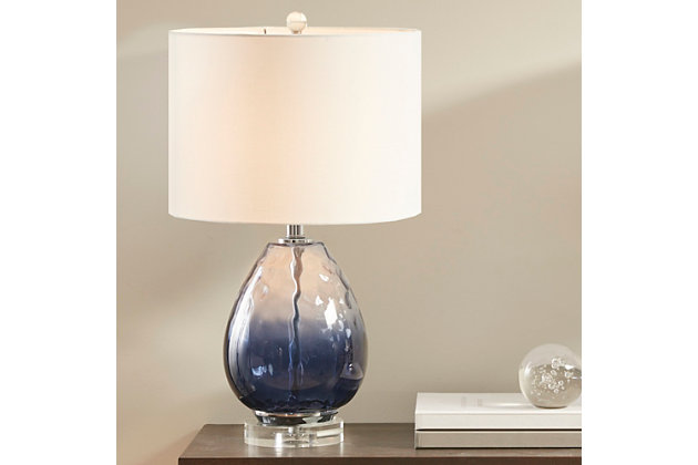 Beautifully designed, the Borel table lamp flaunts a gorgeous blue hue that adds a soft touch of color to your room. The cream-colored, drum-shaped lampshade tastefully accents the base while softly filtering the light to give off a warm glow. The shade also has the ability to tilt, allowing you to easily focus light where you need it. Eye-catching and unique, this table lamp offers a chic update to your space.Made of glass and crystal with drum fabric shade | Blue hue | Metal accents with plated silvertone finish | Tilting shade | On/off switch | 1 E26 socket; incandescent 60-watt or 13-watt bulb recommended (not included) | Power cord included; UL listed | 2-year warranty | Spot clean only | Assembly required