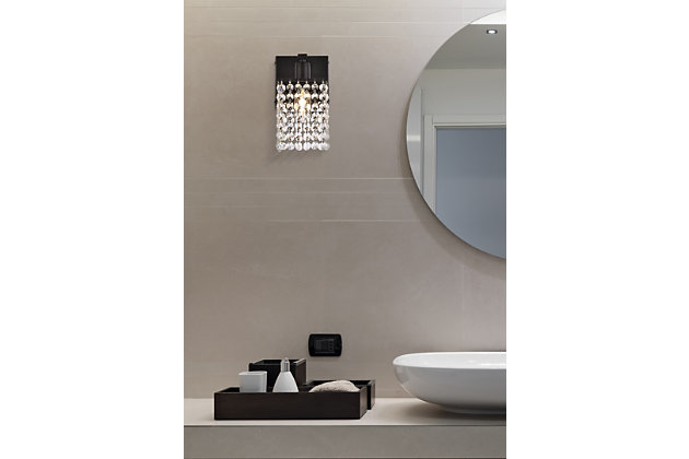 This Phineas Collection sconce exudes elegance and sparkling beauty. Why wouldn't it, with its beautiful curtain of clear crystal strands that shimmer with each passing second as light passes through? Your home will be illuminated and your guests will be charmed by these dancing crystal lights. And you'll be pleased with how this wall lamp can elevate any room into a luxurious and glamourous world.Made of crystal and iron | Glamourous and ritzy wall sconce sparkles with cool ease | Curtains of clear crystals | Light illuminates downwards (and is dimmable) | Uses E12 bulb (sold separately); compatible with LED bulbs | Easily mounted on wall | No assembly required | Imported