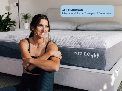 Model wearing white top and jeans sitting on edge of bed with Molecule logo
