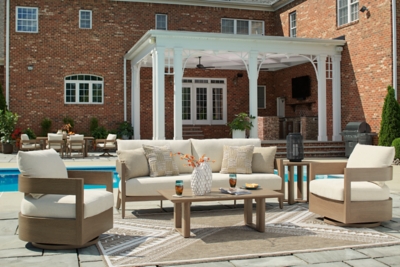 Patio seating area with sofa and chairs arranged around a coffee table under a pergola