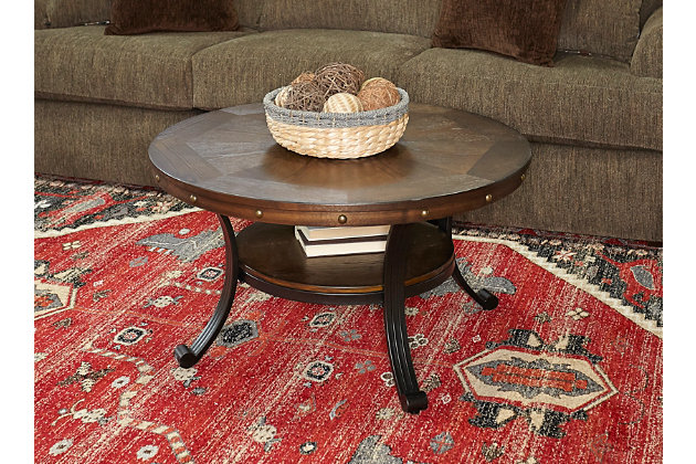 A beautiful mixture of metal metal and wood, this transitional coffee table provides a unique addition to your home. The round table features an oak woodgrain veneer finish with nailheads along the apron. The sturdy metal base includes curved legs and a small lower shelf that add dimension to the design.Made of engineered wood, oak, veneer and metal | Oak woodgrain veneer finish | Antiqued brass-tone nailheads | Metal legs with black finish | Assembly required